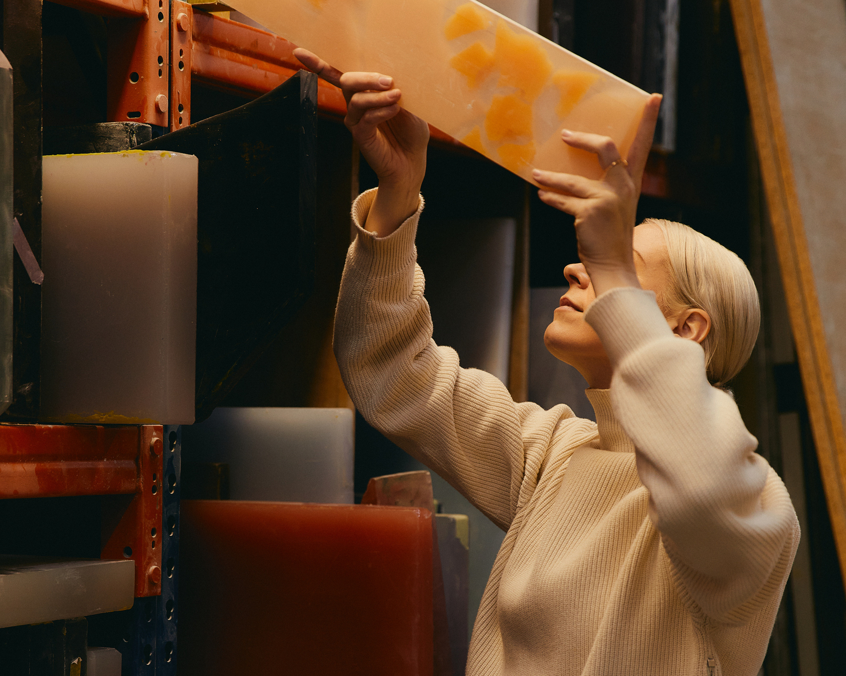 Person in a workshop taking a colored piece of material from a shelf.