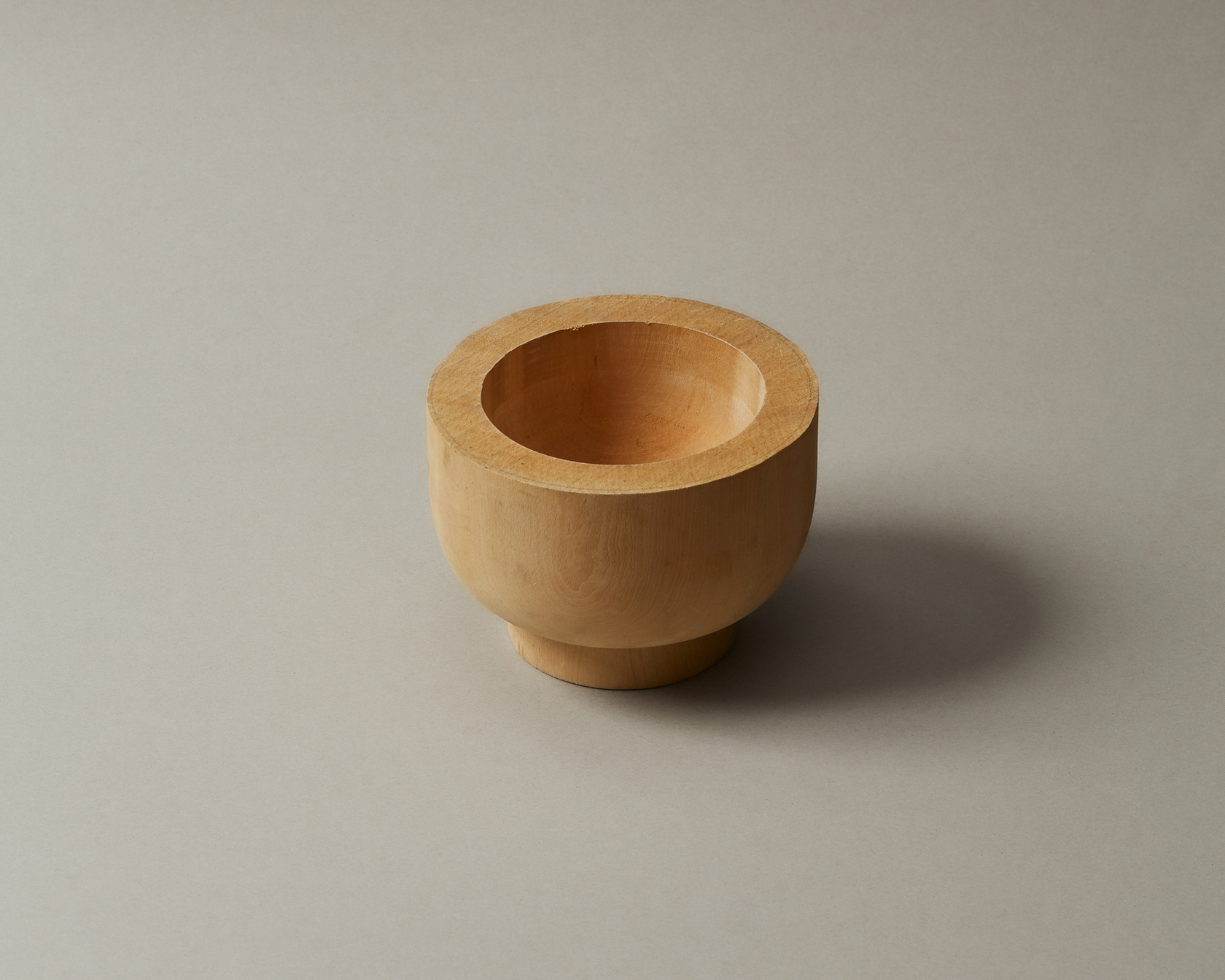 Minimalist wooden bowl made of light-colored wood on a neutral background.