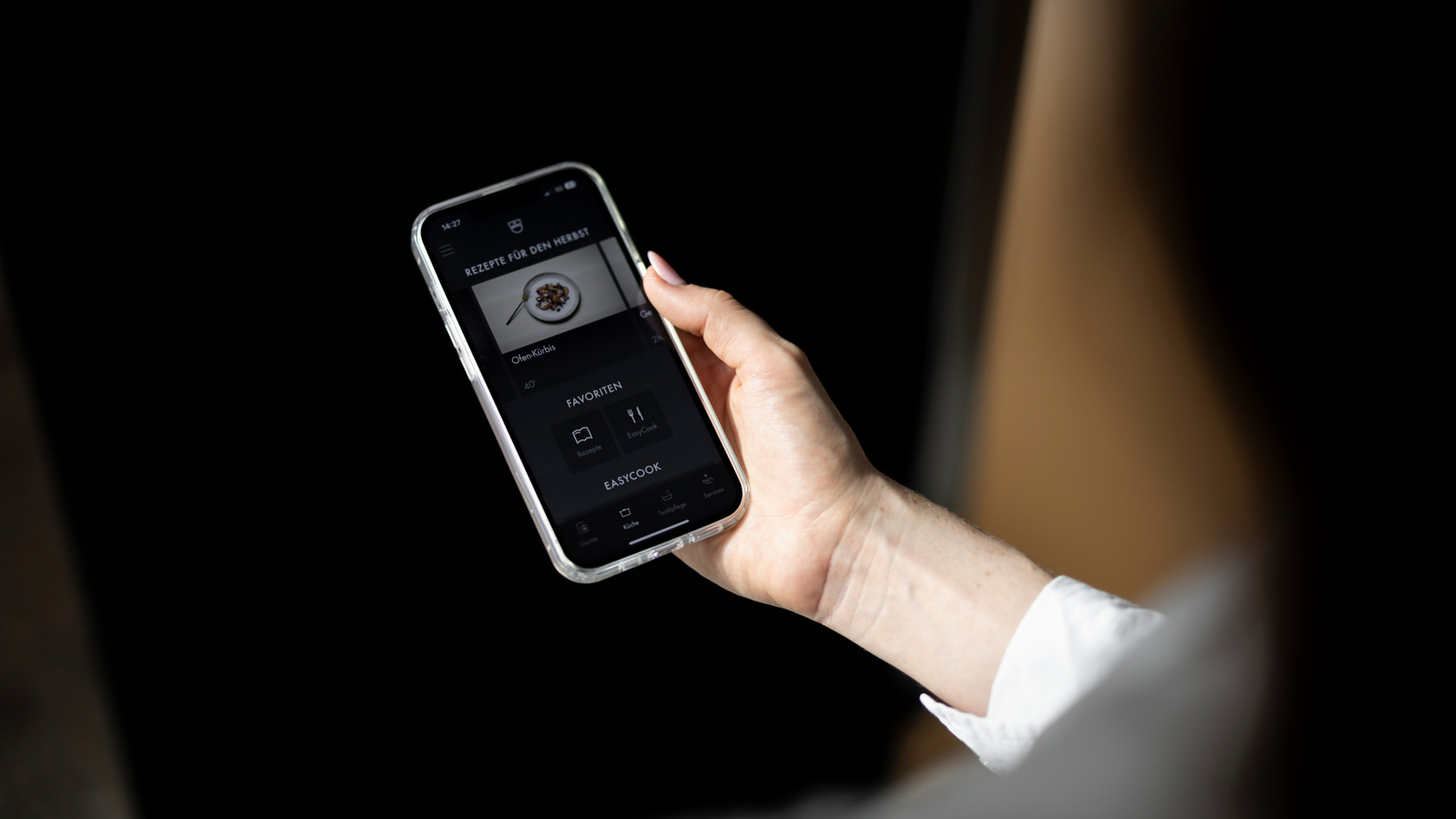 La main tient le smartphone avec l'application de recette ouverte, qui affiche un plat et des options de sélection.