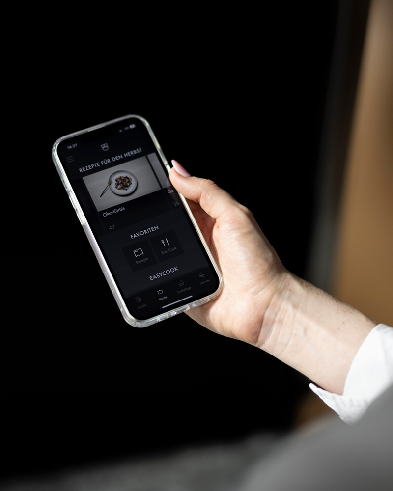 Hand holding smartphone with recipe app open, displaying a dish and selection options.