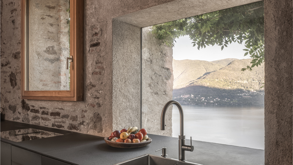 Cucina moderna con parete in pietra, piano di lavoro nero e vista sul lago