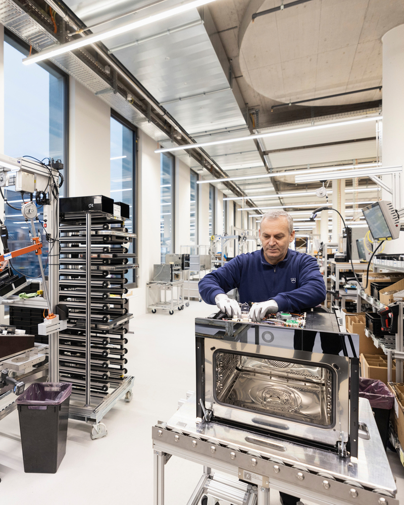 Assembly of an oven in a modern production area with shelves and tools in the background.