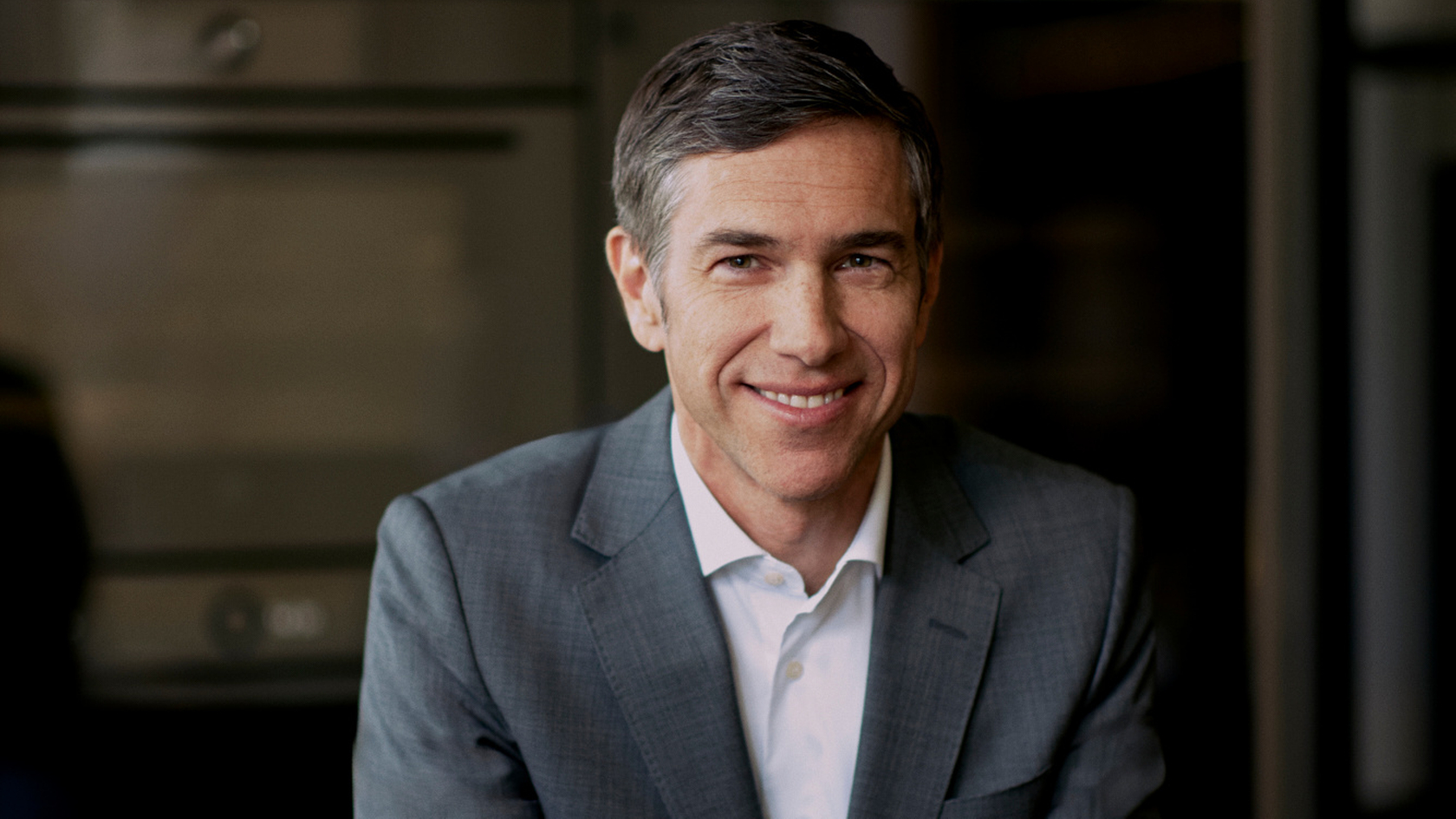 Man in gray suit at modern kitchen island with oven in the background