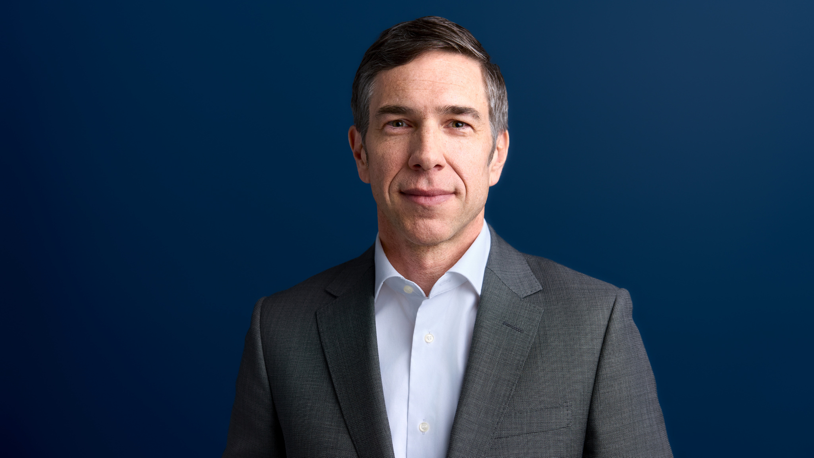 Portrait of a man in a gray suit against a blue background