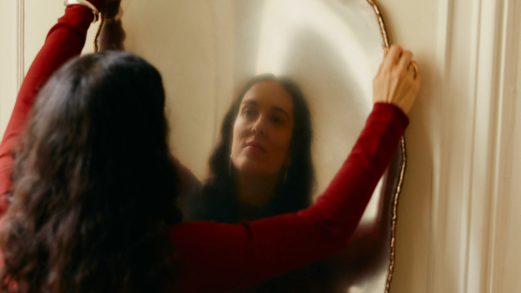 Woman holding an organically shaped mirror in front of a wall