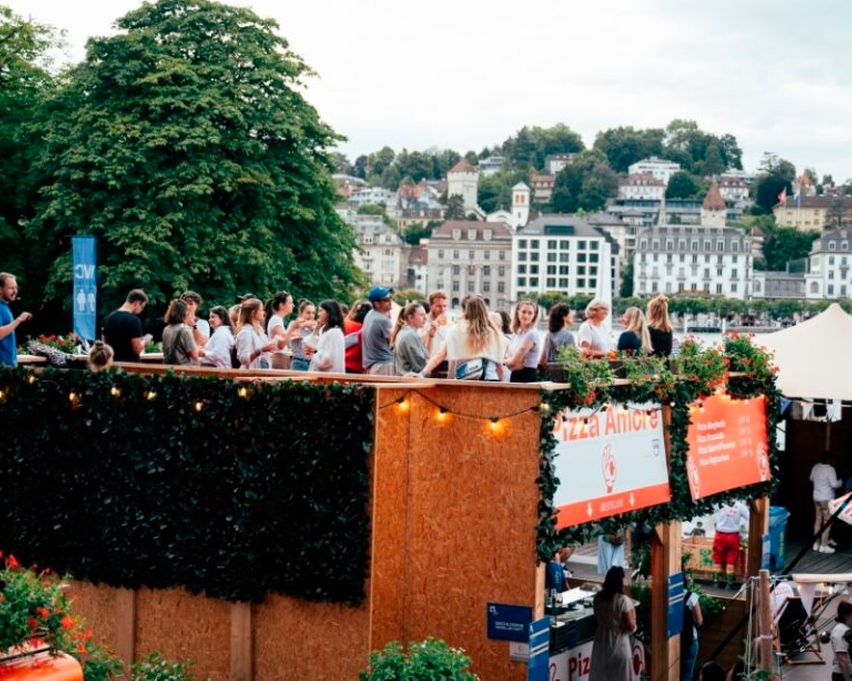 Gruppe von Menschen auf einer Terrasse bei einer sommerlichen Veranstaltung mit Blick auf eine Stadtlandschaft
