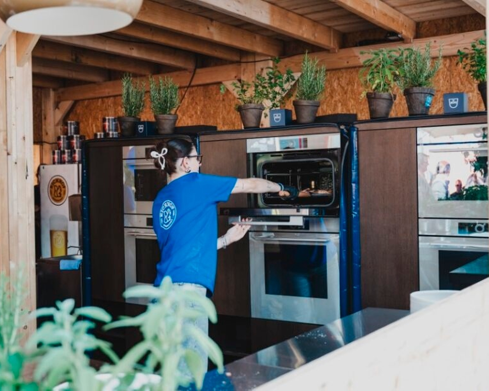 Person öffnet Backofen in moderner Küche mit Kräutertöpfen