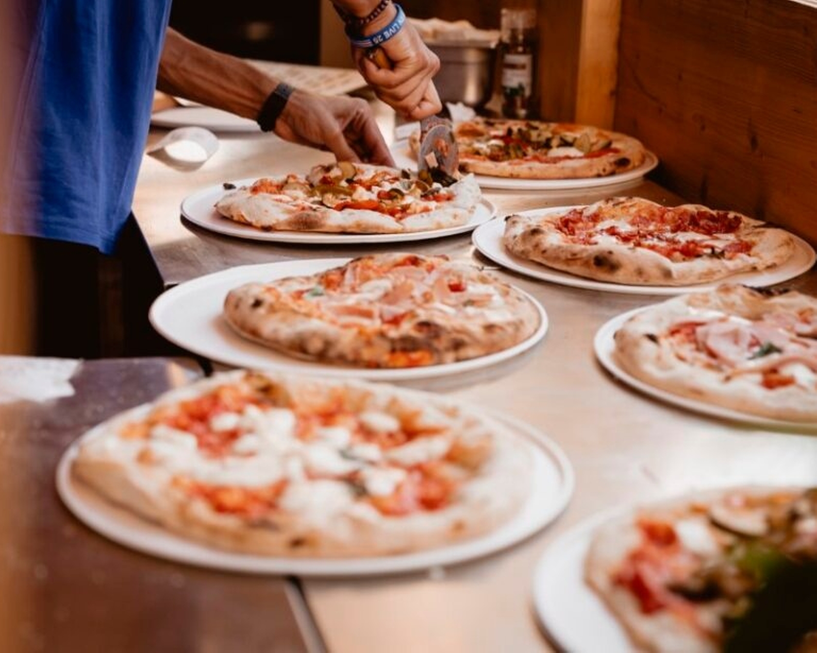 Frisch gebackene Pizzen auf Tellern in einer Küche, eine Person schneidet eine Pizza mit einem Pizzaschneider.