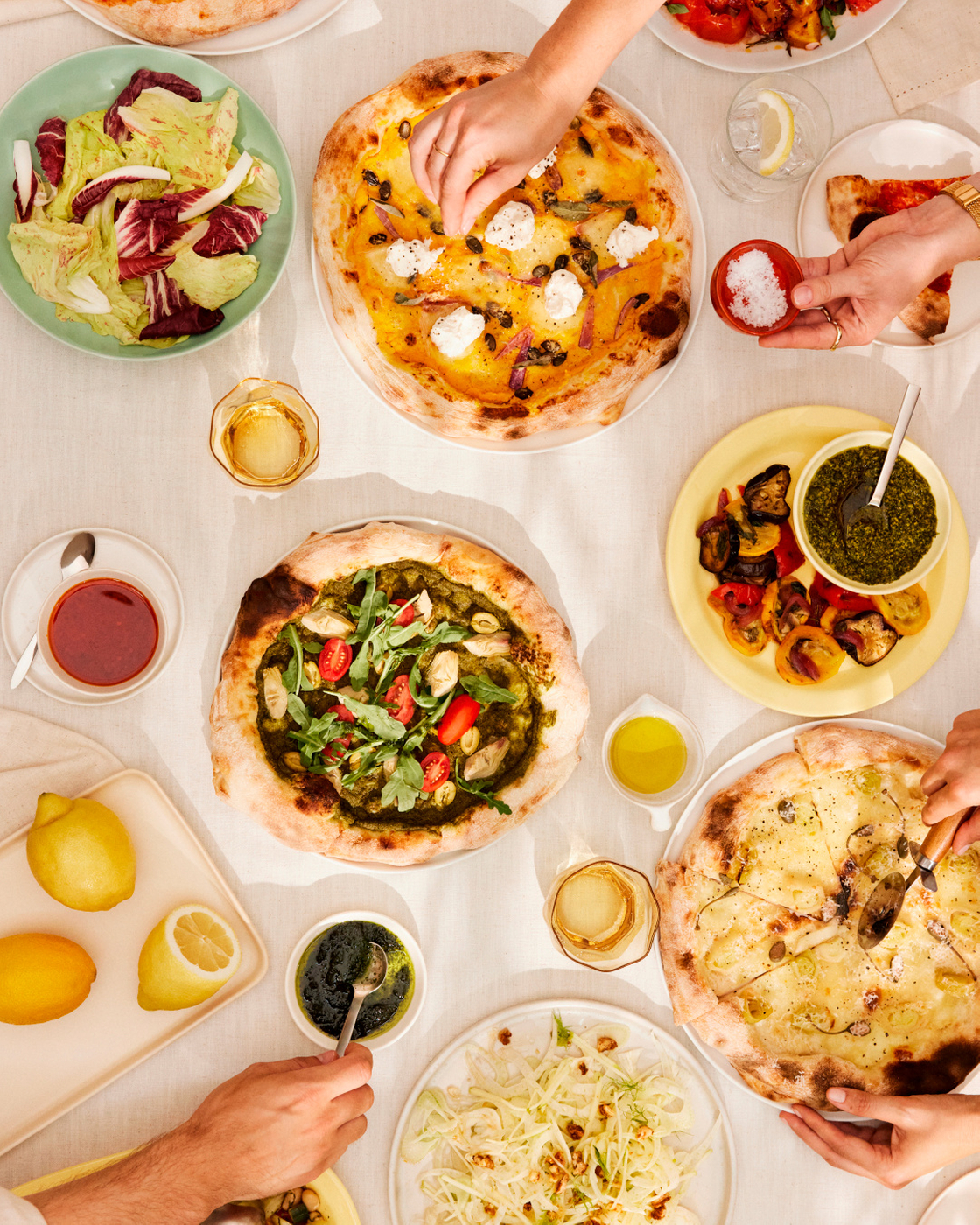 Set table with pizzas, salad and side dishes in an inviting dining scene.