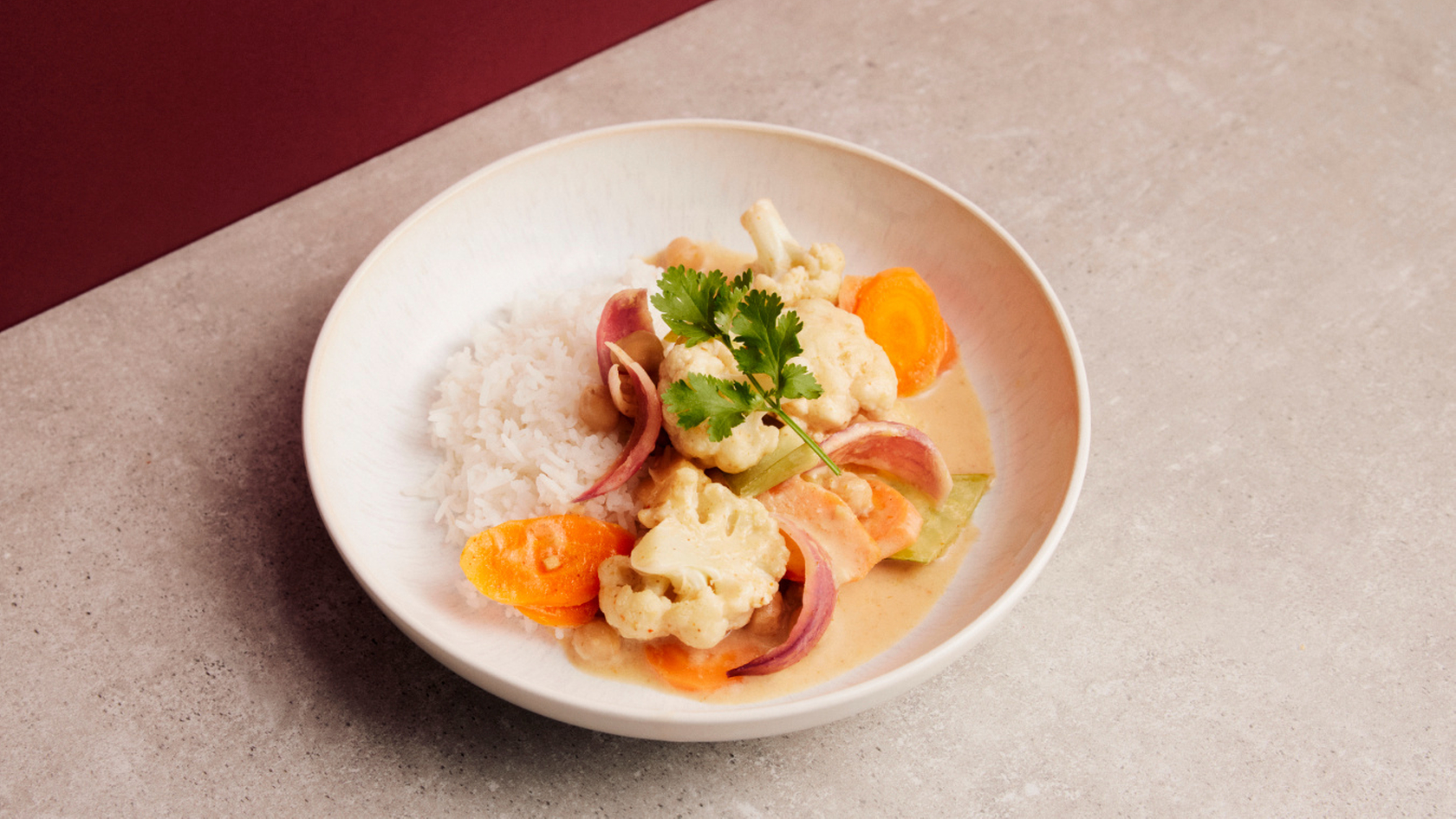 Gemüse-Curry mit Reis auf einem Teller, angerichtet mit frischen Kräutern.