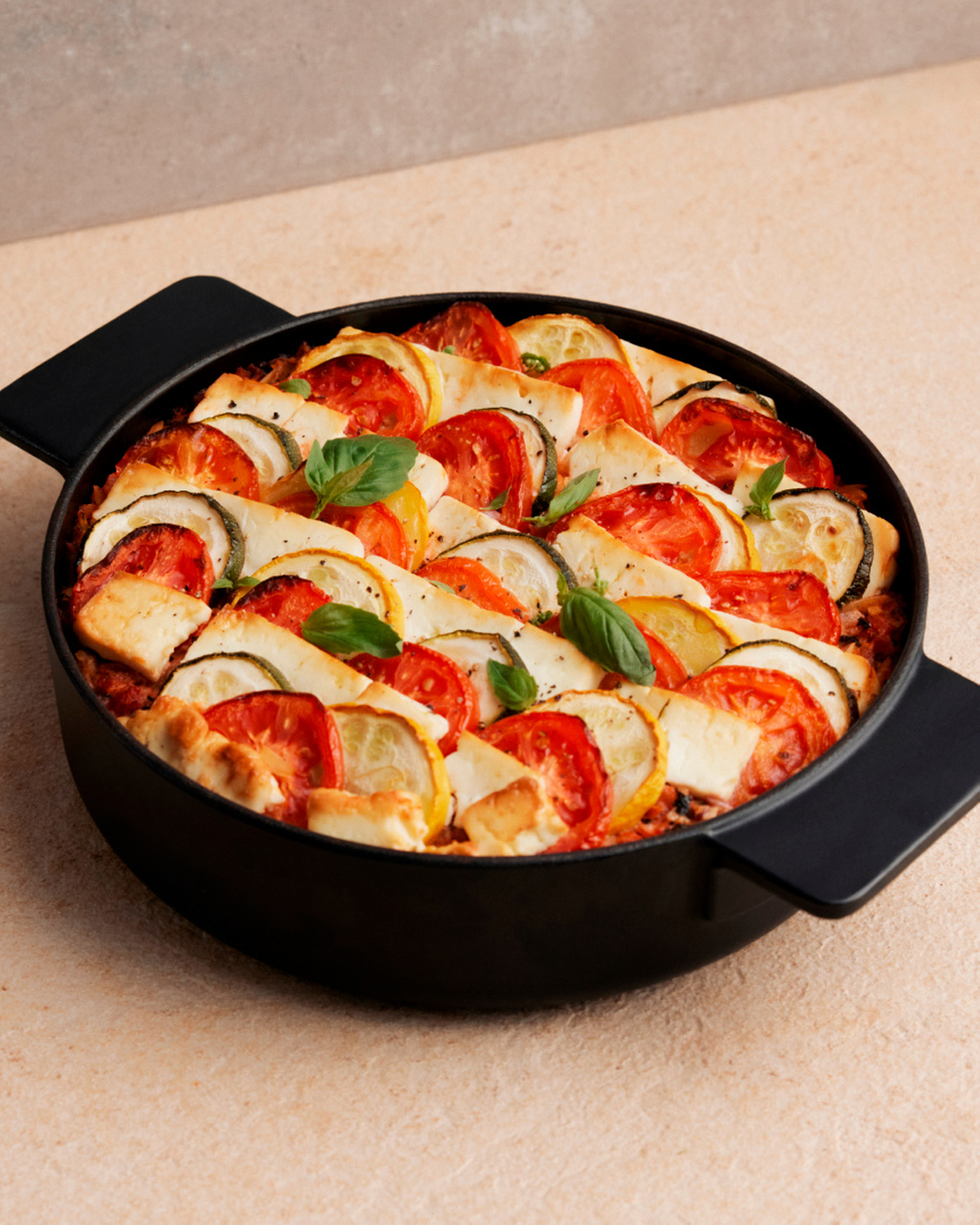 Frisch gebackener Gemüseauflauf mit Tomaten, Zucchini und Käse in einer schwarzen Auflaufform.