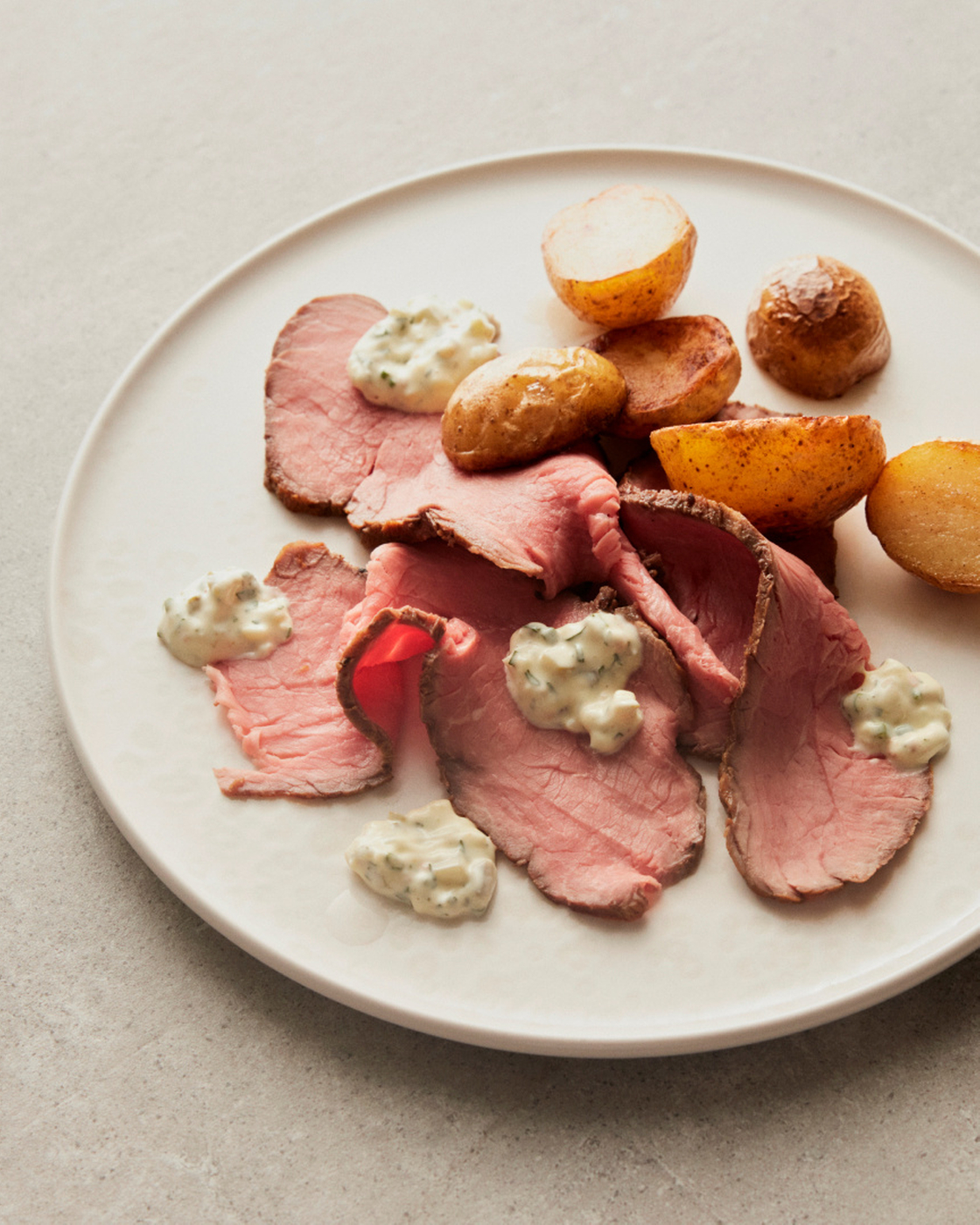 Roast beef with potatoes and herb sauce on a white plate