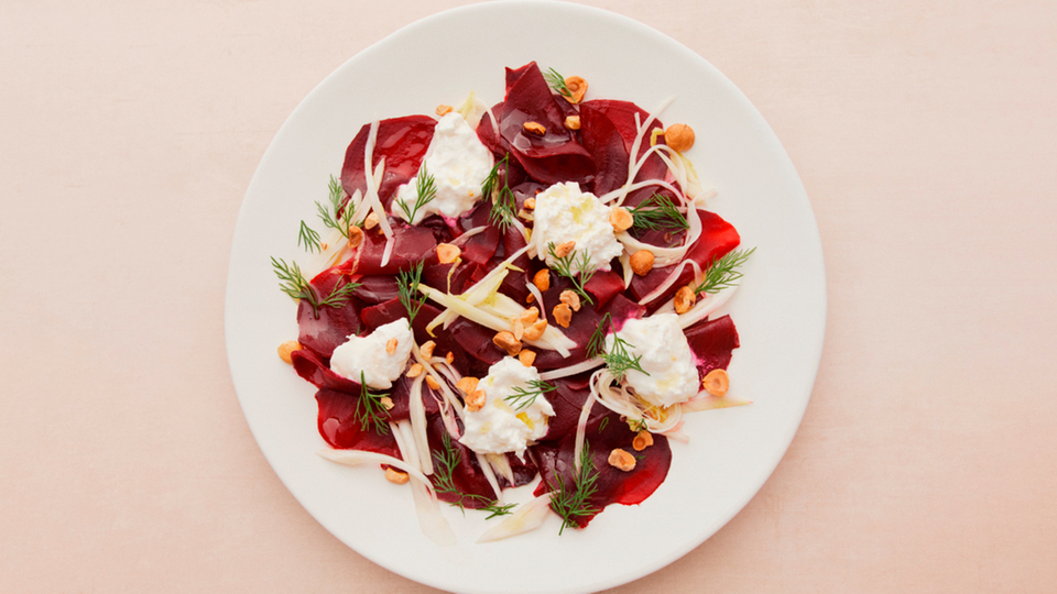 Beet carpaccio with cream cheese, dill and hazelnuts on a white plate