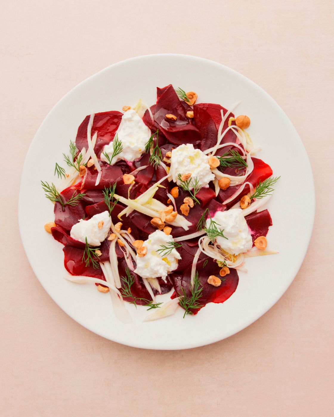 Beet carpaccio with cream cheese, dill and hazelnuts on a white plate