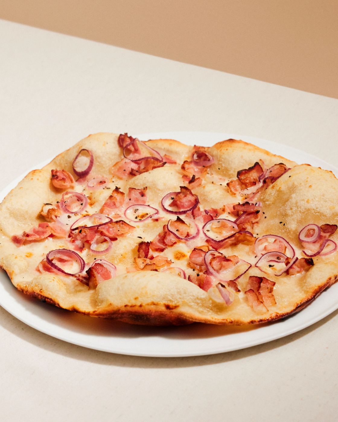 Tarte flambée with bacon and red onions on a white plate, perfectly baked.