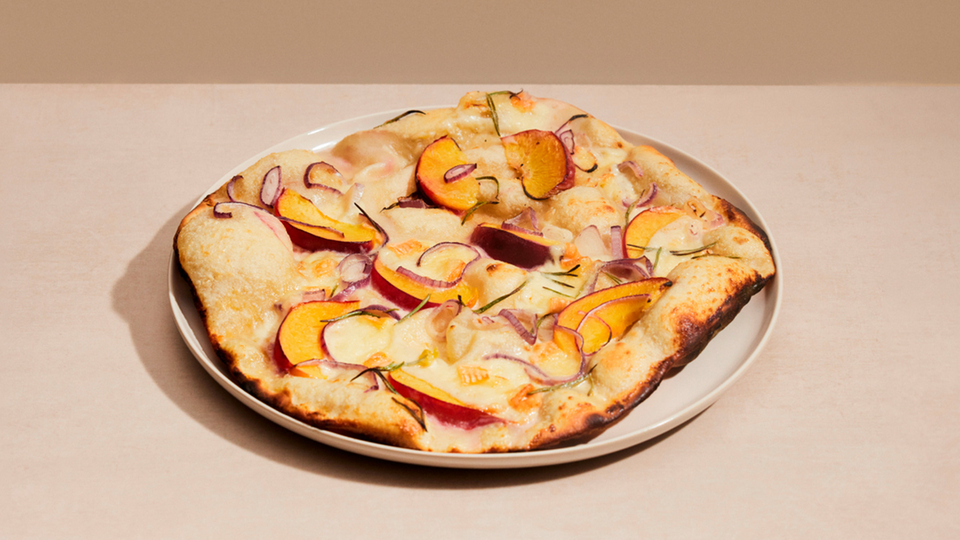 Tarte flambée with peach, red onions and rosemary on a white plate.