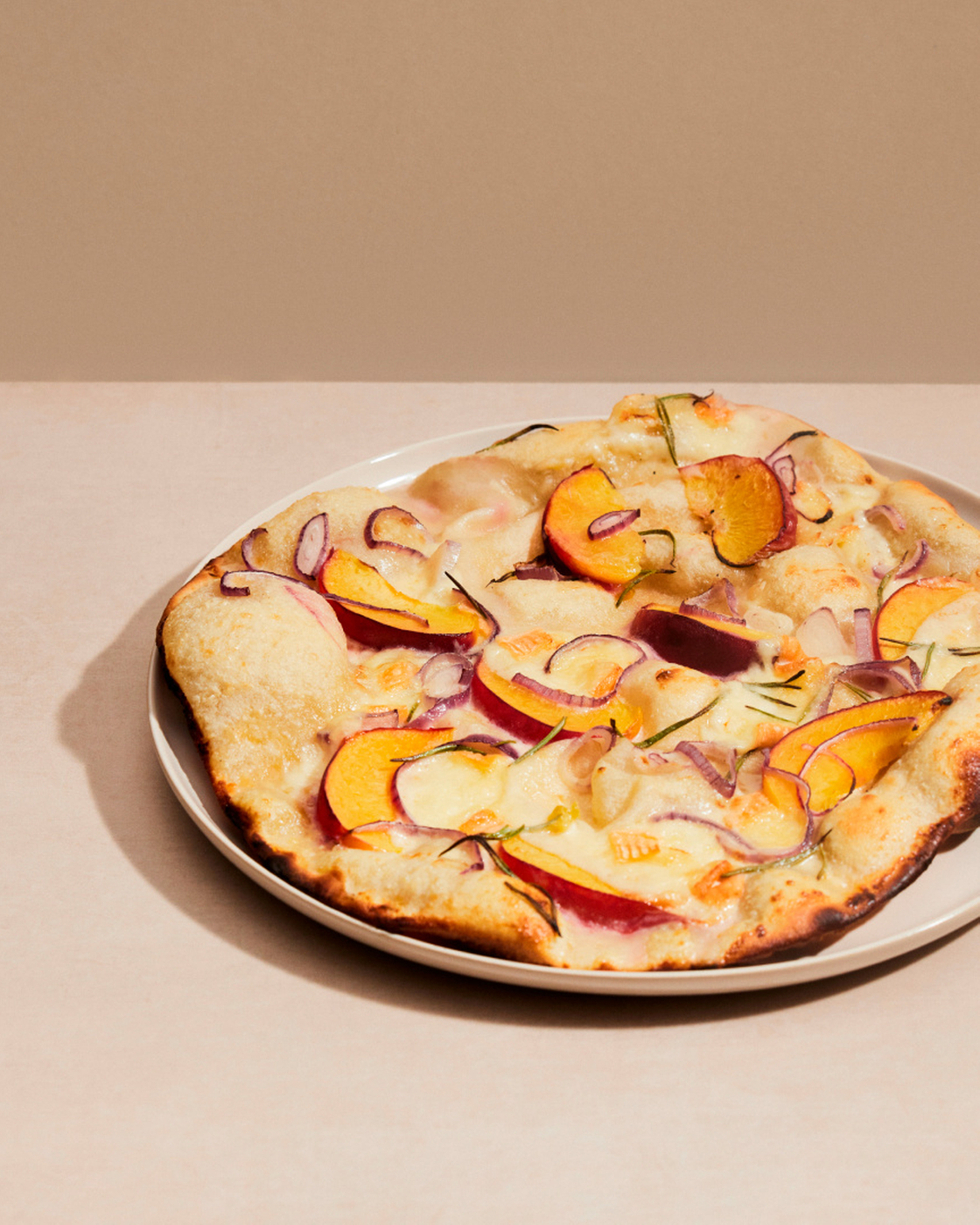 Tarte flambée with peach, red onions and rosemary on a white plate.