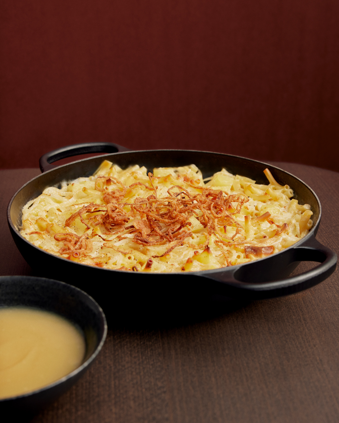 Cheese spaetzle in a black pan with fried onions on a dark table