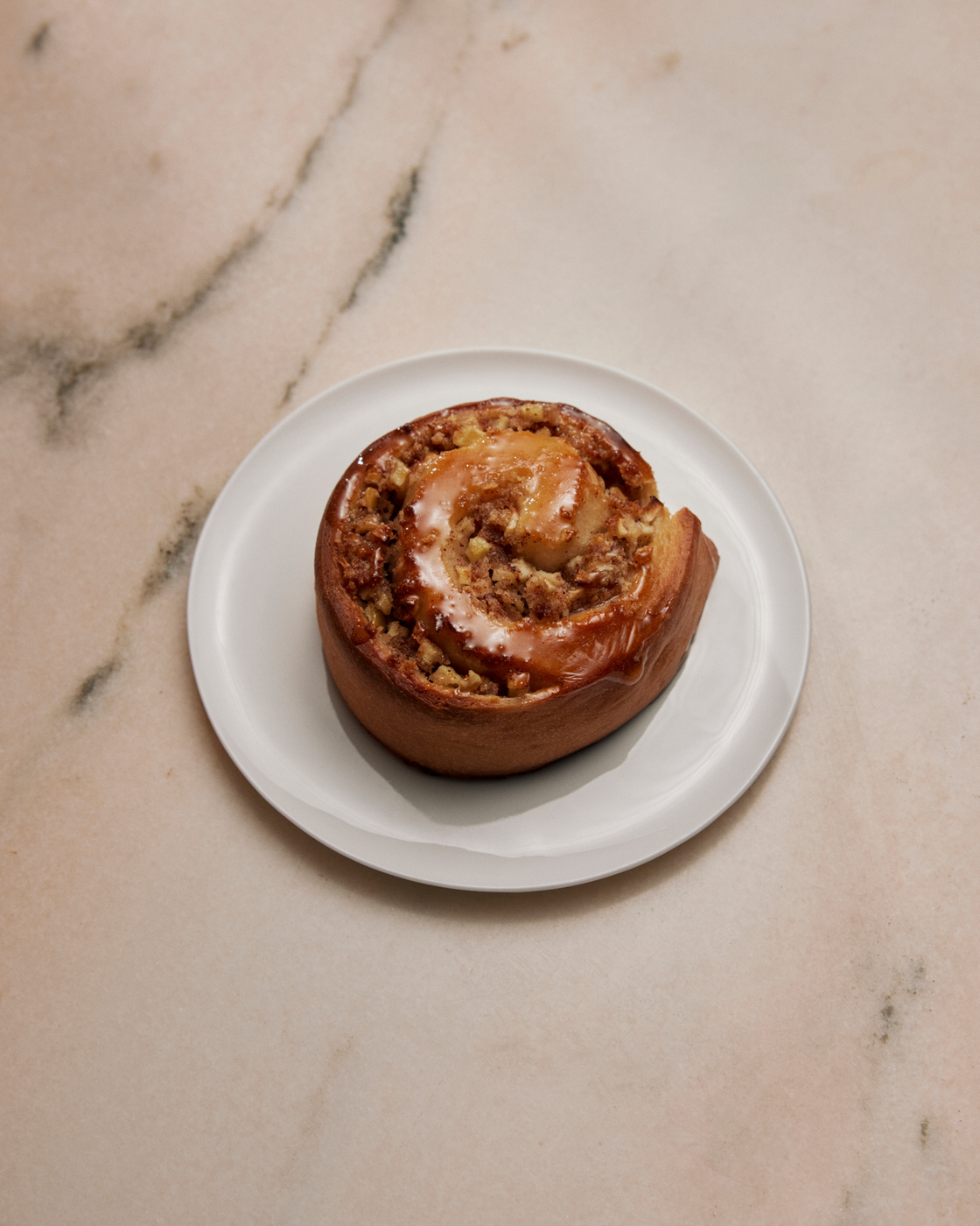 Freshly baked cinnamon bun with glaze on a white plate on a marble table