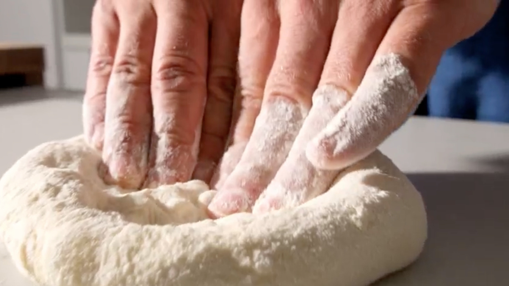 Hands kneading fresh dough on a work surface in the kitchen.