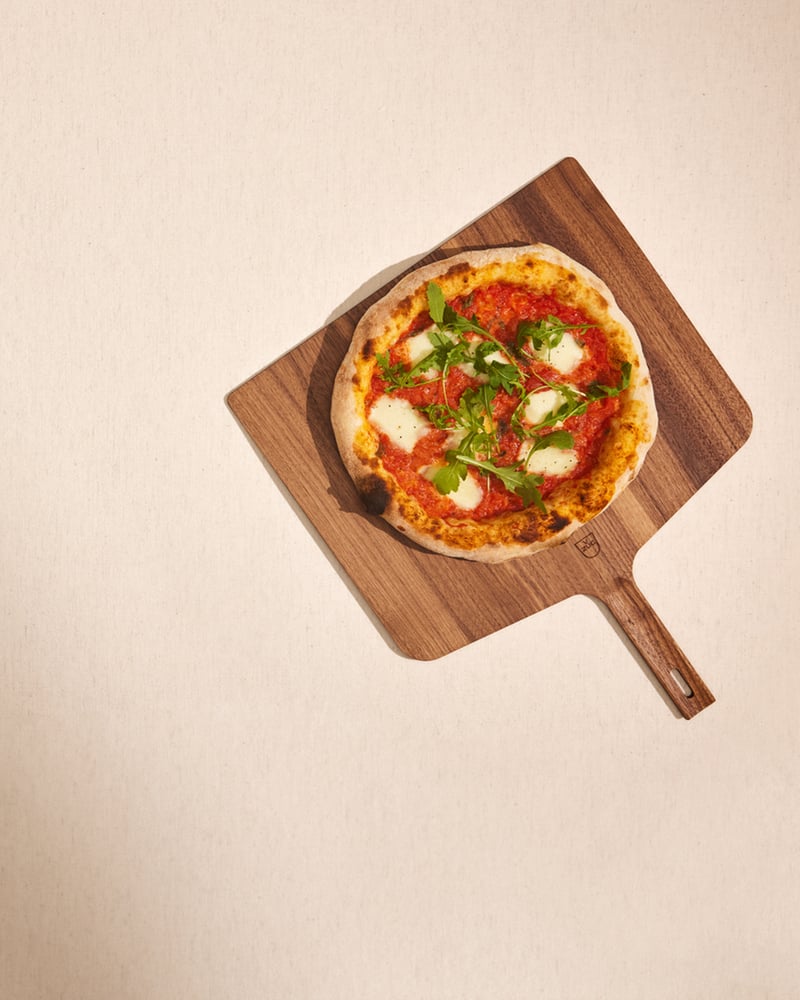 Pizza Margherita auf einem Holzbrett mit frischen Kräutern