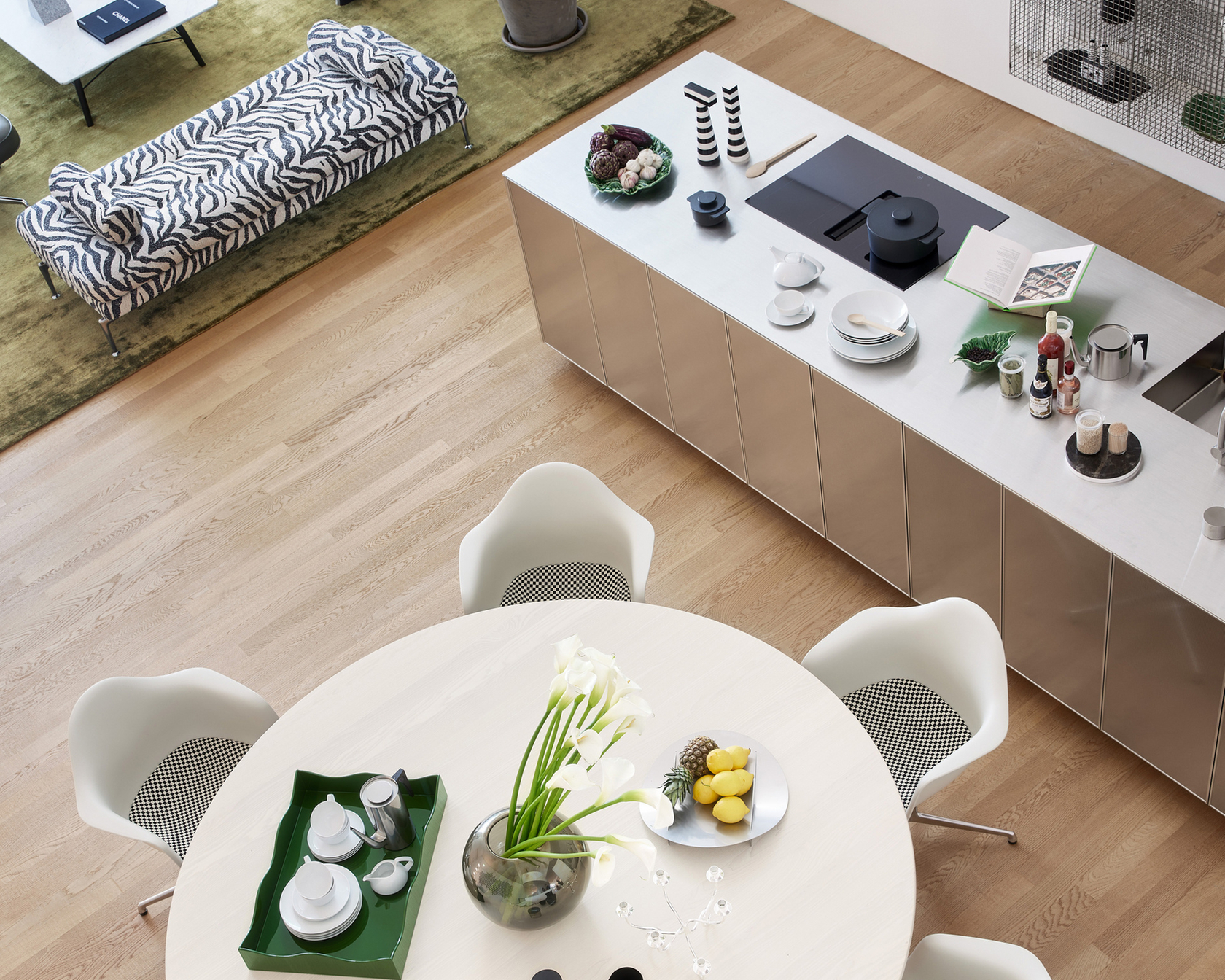 Modern kitchen with stainless steel cooking island and round dining table, decorated with flowers and fruit.