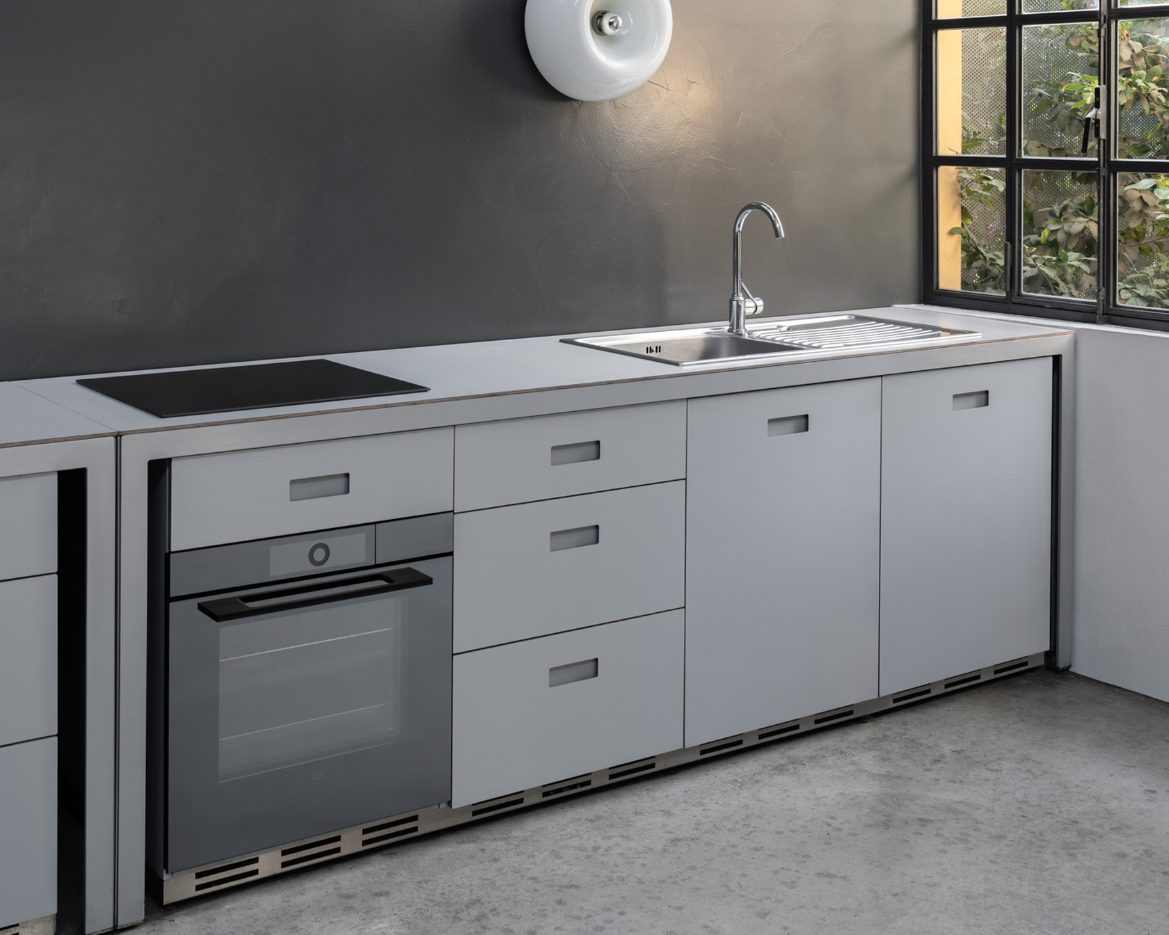 Moderne Küche mit grauen Schränken, Backofen und Kochfeld neben einem großen Fenster