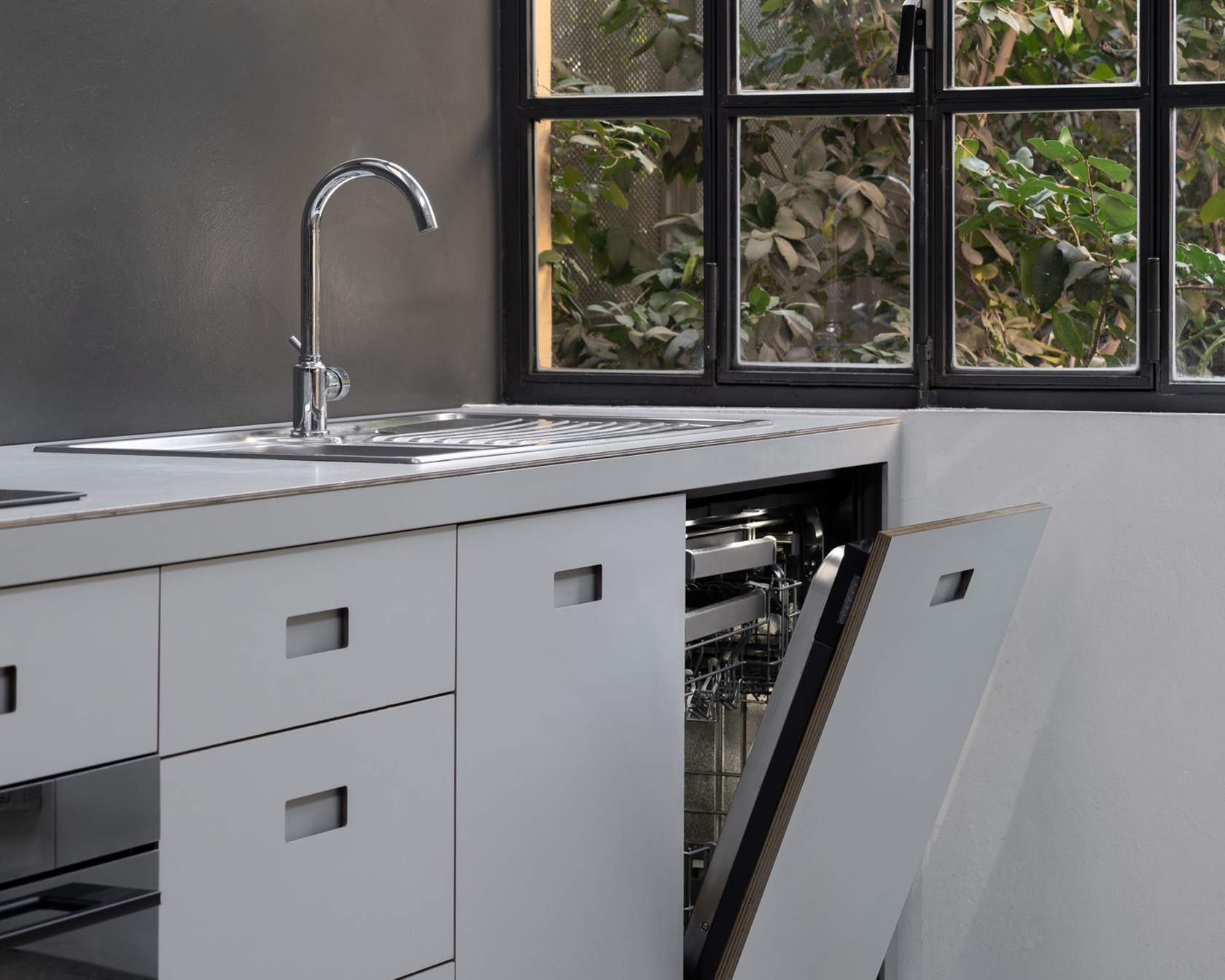 Moderne Küche mit eingebautem Geschirrspüler und Blick auf grüne Pflanzen durch ein großes Fenster
