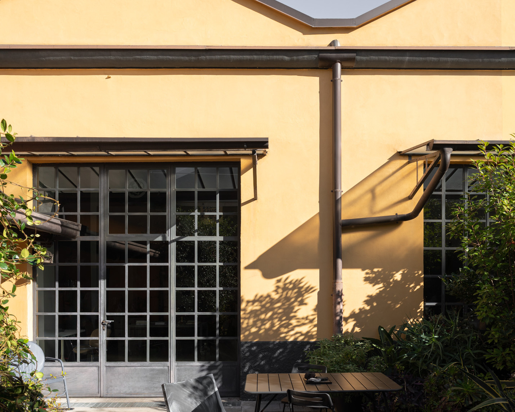 Gelbe Fassade mit Terrasse, modernen Gartenmöbeln und Pflanzen im Sonnenlicht.