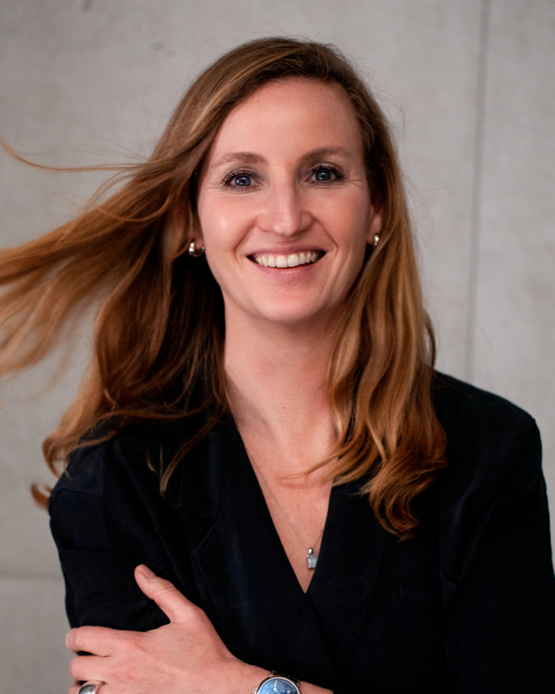 Woman with brown hair and black outfit in front of concrete wall