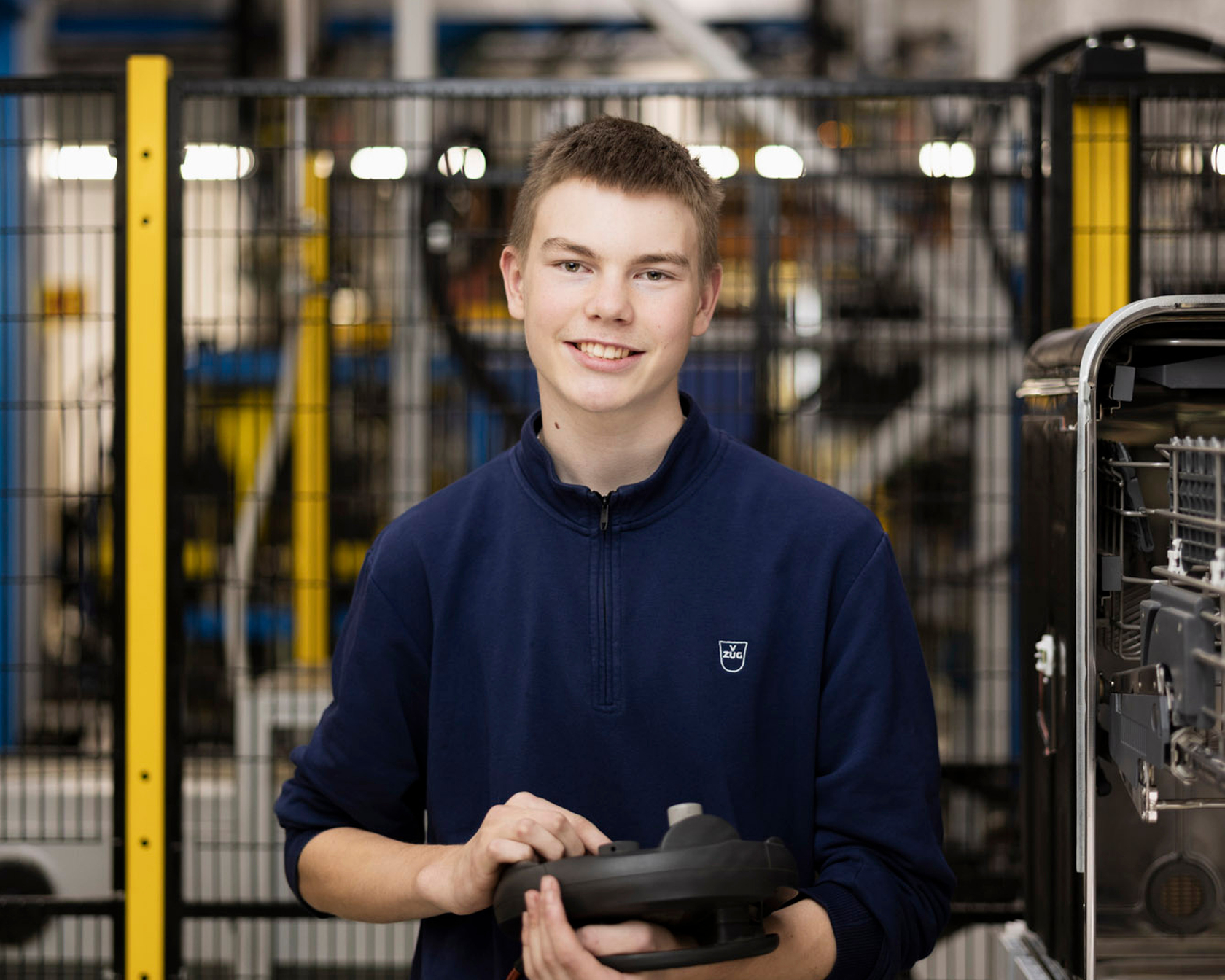 Dipendenti in un ambiente di produzione con un componente in mano, circondati da macchine e sistemi.