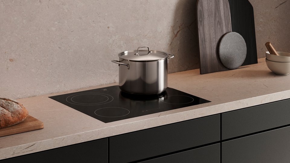 Cuisine moderne avec plaque de cuisson à induction, casserole en inox et ustensiles de cuisine élégants sur plan de travail clair.