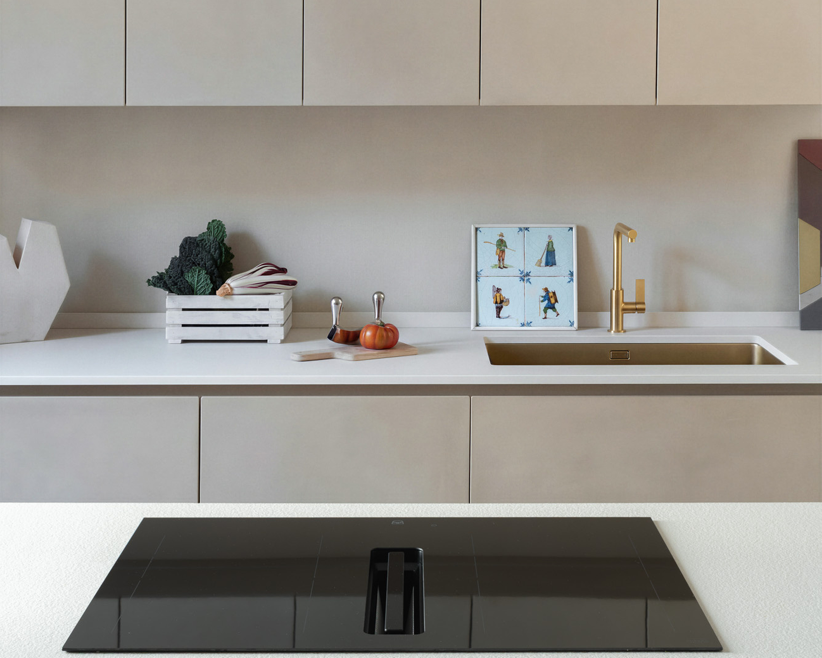Modern kitchen with black hob and integrated extractor fan, gold fittings and bright worktop.