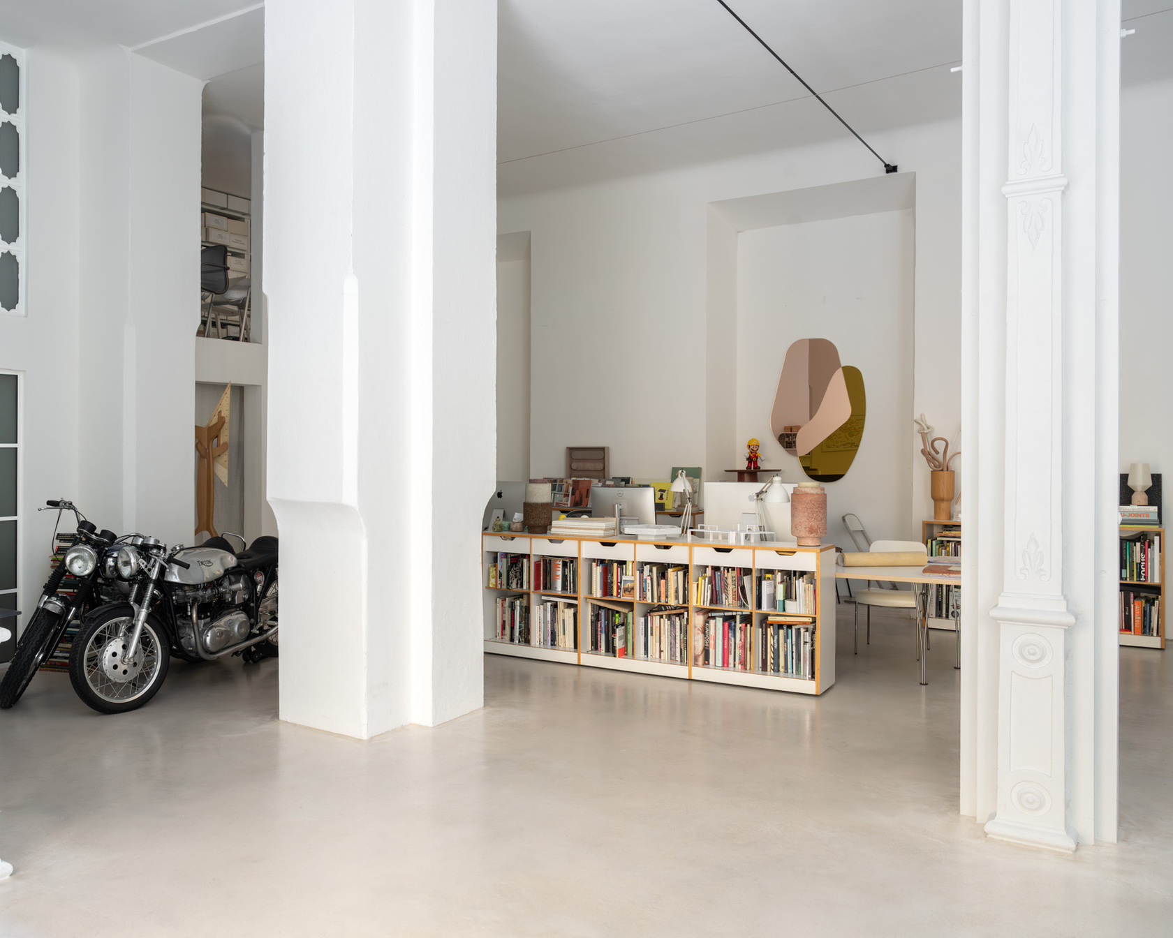 Interior with motorcycle, bookcase and modern furniture in a bright room with white columns.