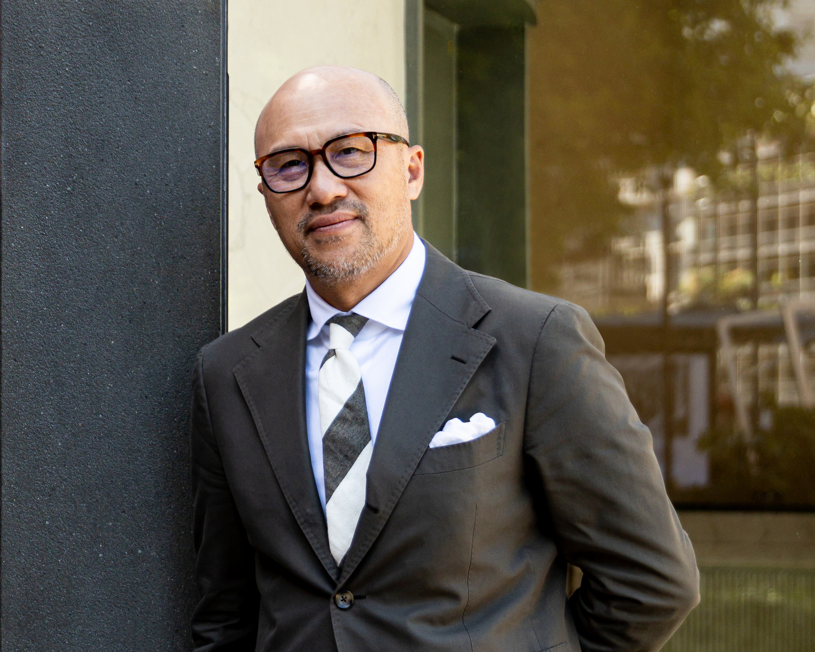 Man in a black suit in front of a modern building with a glass facade
