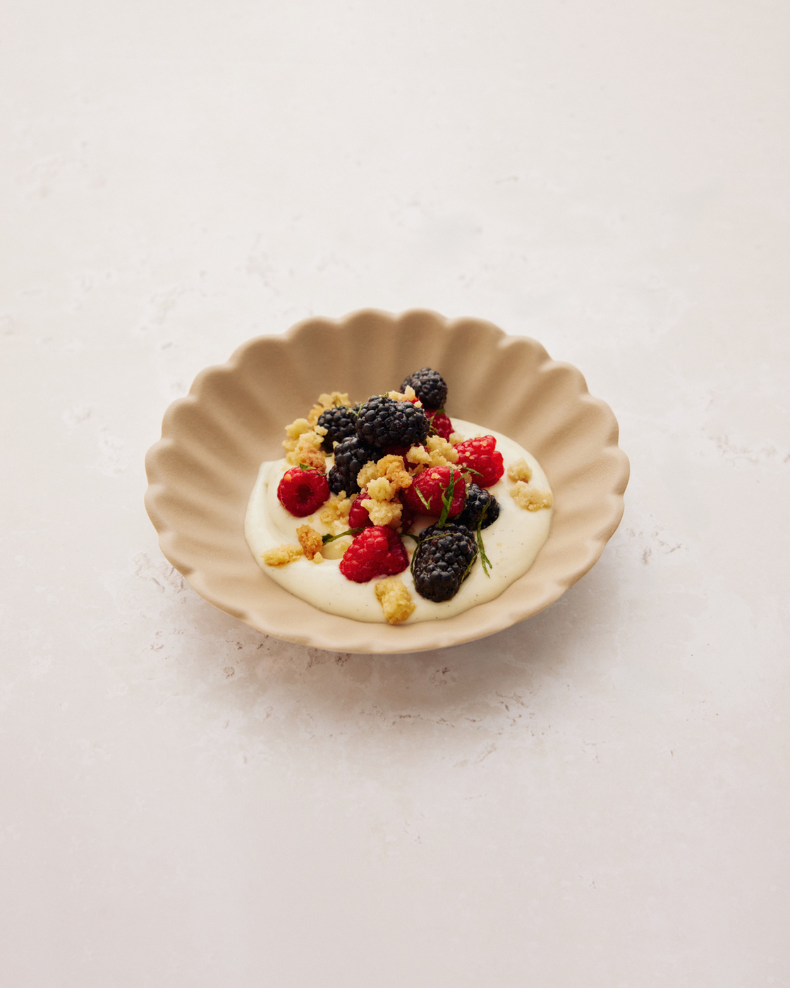 Dessert with fresh berries, crumble and cream in a decorative bowl.