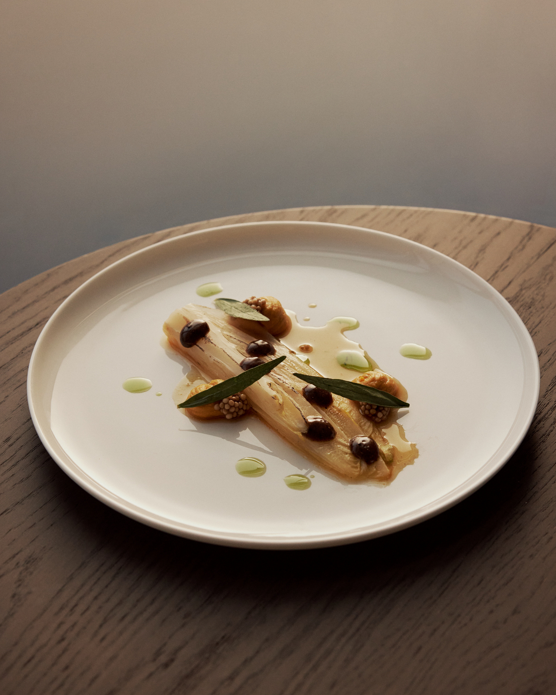 Elegant dish on a white plate, decorated with herbs and sauces, on a wooden table.