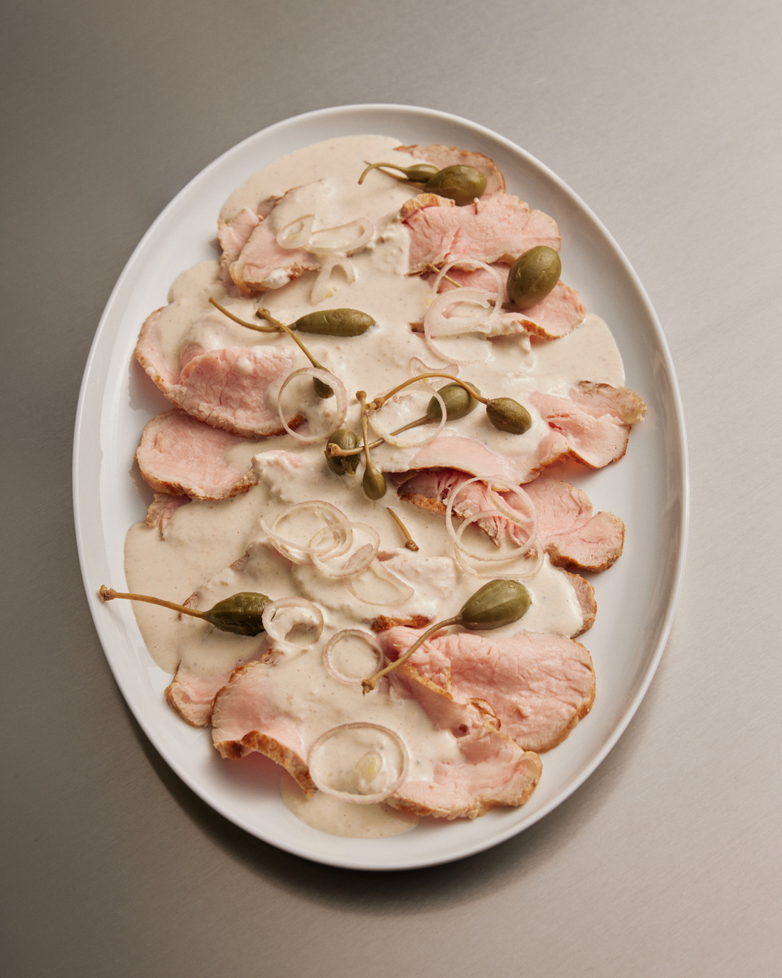 Vitello tonnato on a white plate, served with capers and tuna sauce.