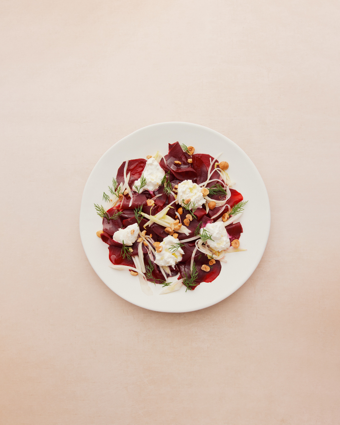 Beet salad with cream cheese, dill and nuts on a white plate.