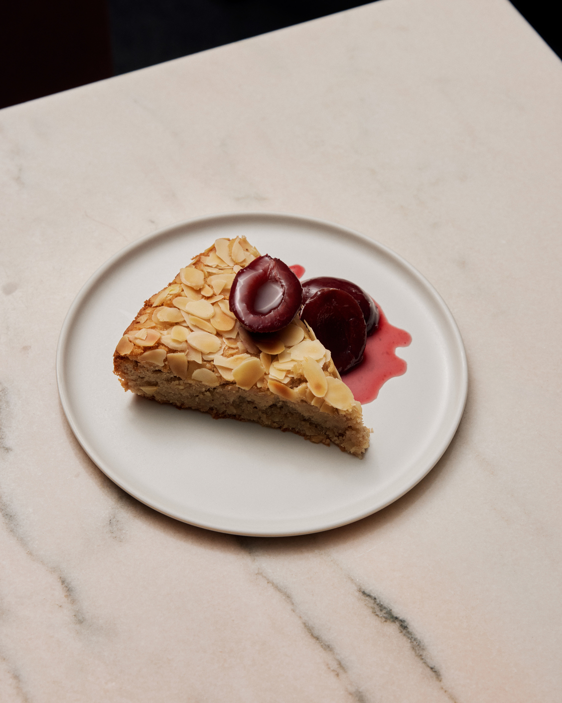 Mandelkuchen mit Kirschen und Kirschsoße auf einem Teller, präsentiert auf einer Marmoroberfläche.