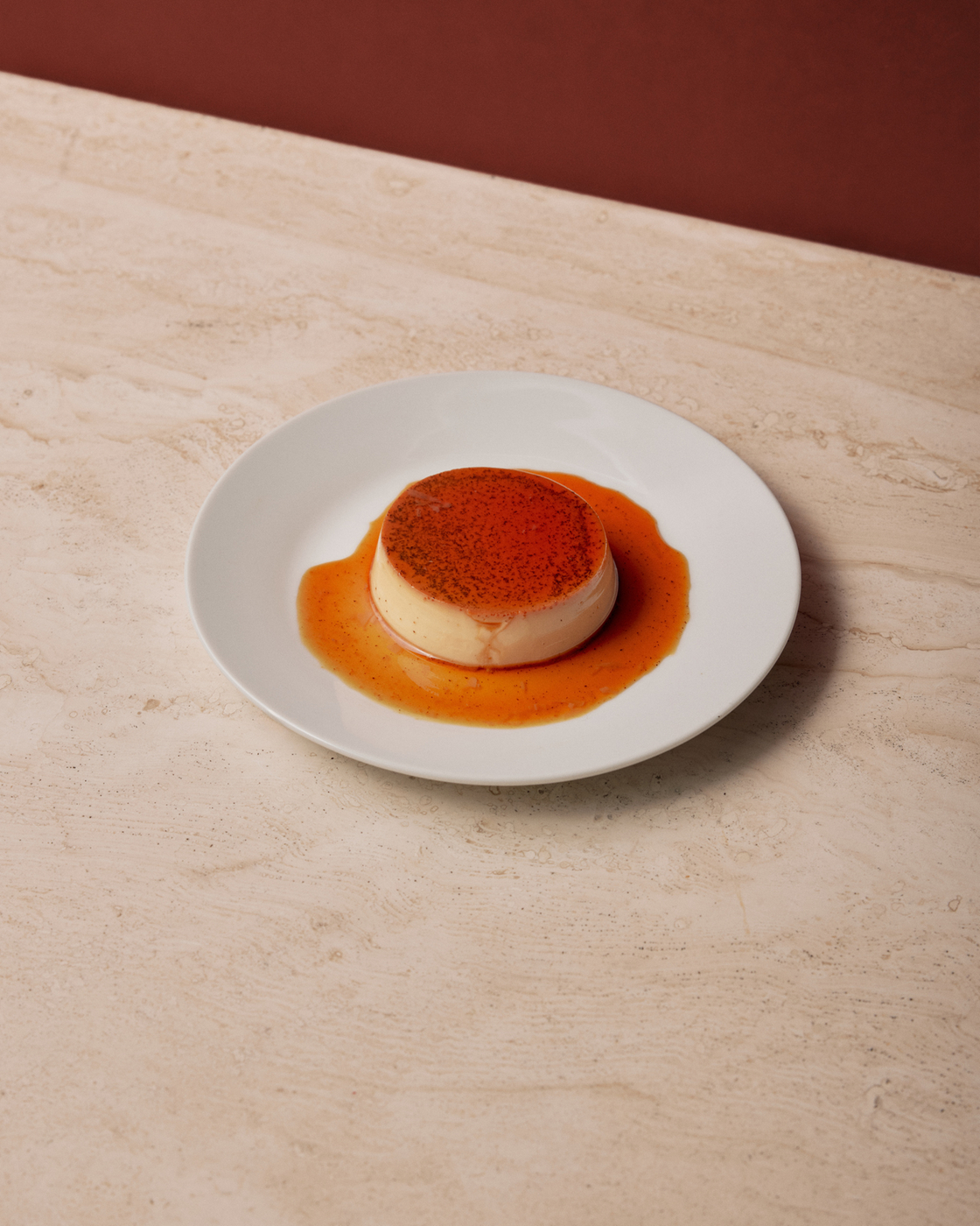 Karamell-Dessert auf einem weißen Teller vor rotem Hintergrund
