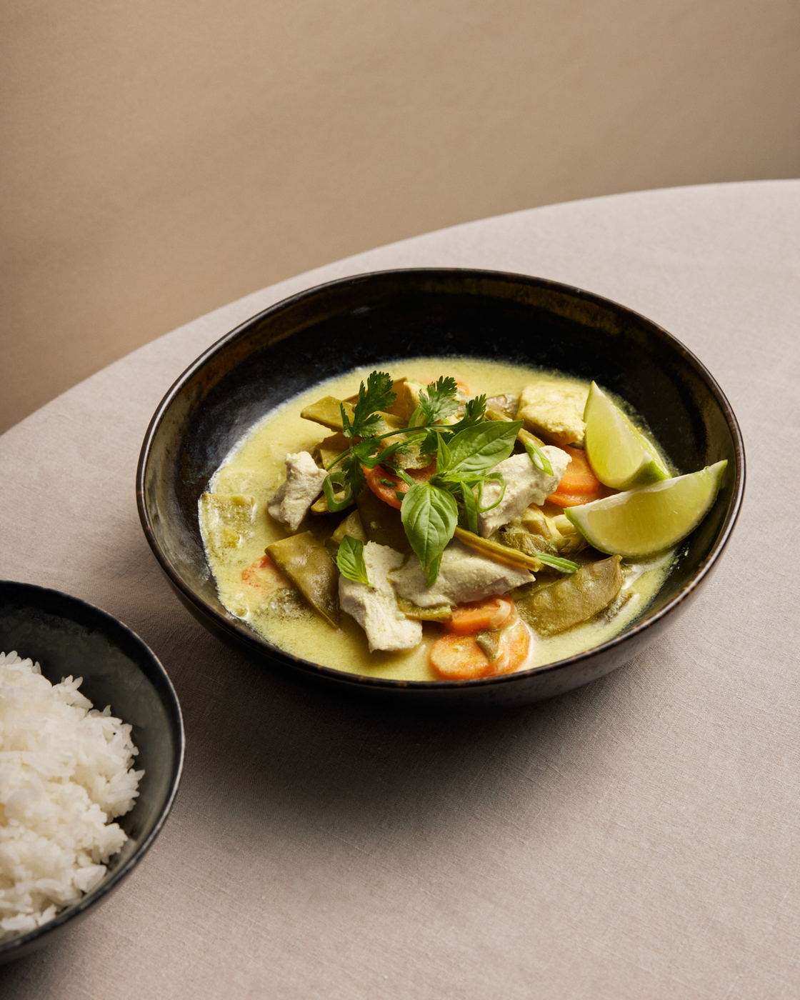 Grünes Curry mit Hähnchen, Gemüse und Reis auf einem Tisch.