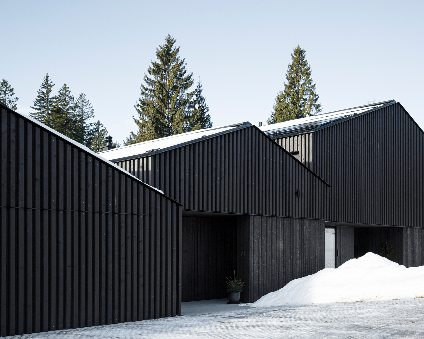 Schwarzes modernes Haus mit Holzfassade in einer verschneiten Landschaft.