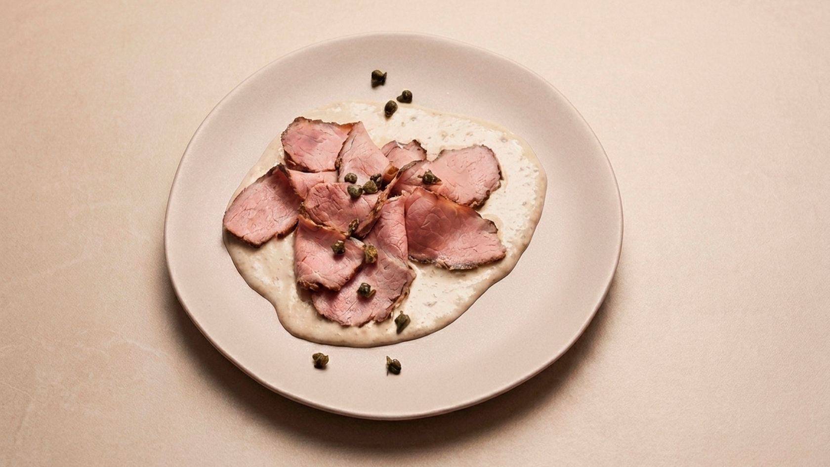 Vitello Tonnato served on a plate with capers as garnish.