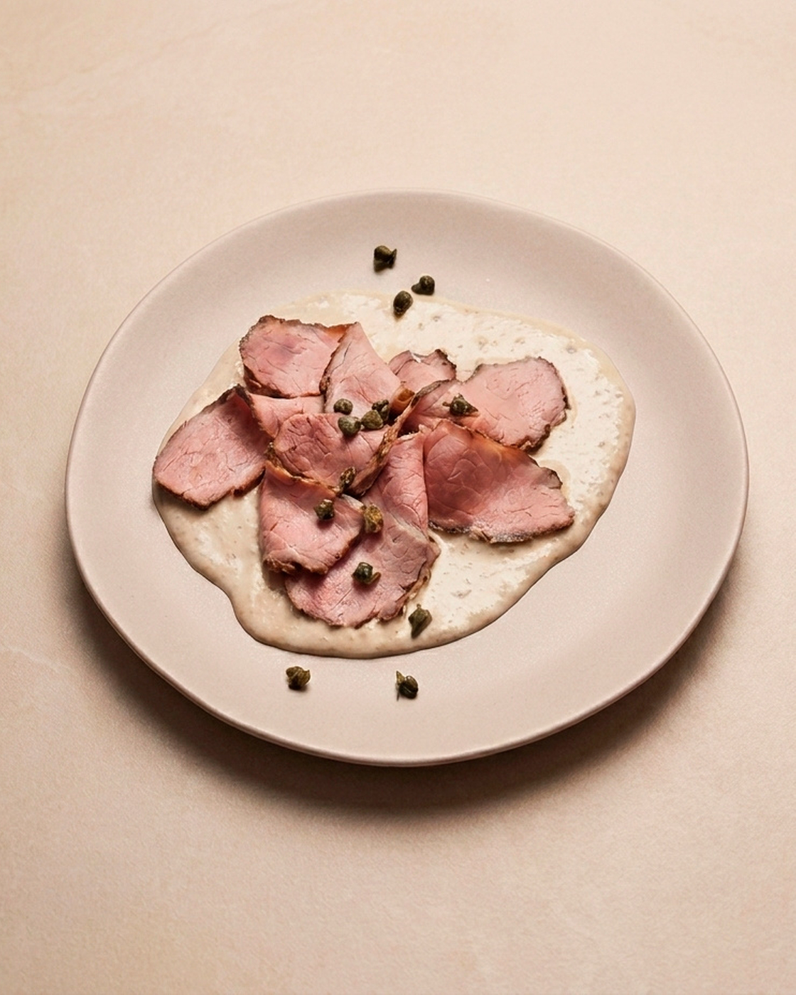 Vitello Tonnato served on a plate with capers as garnish.