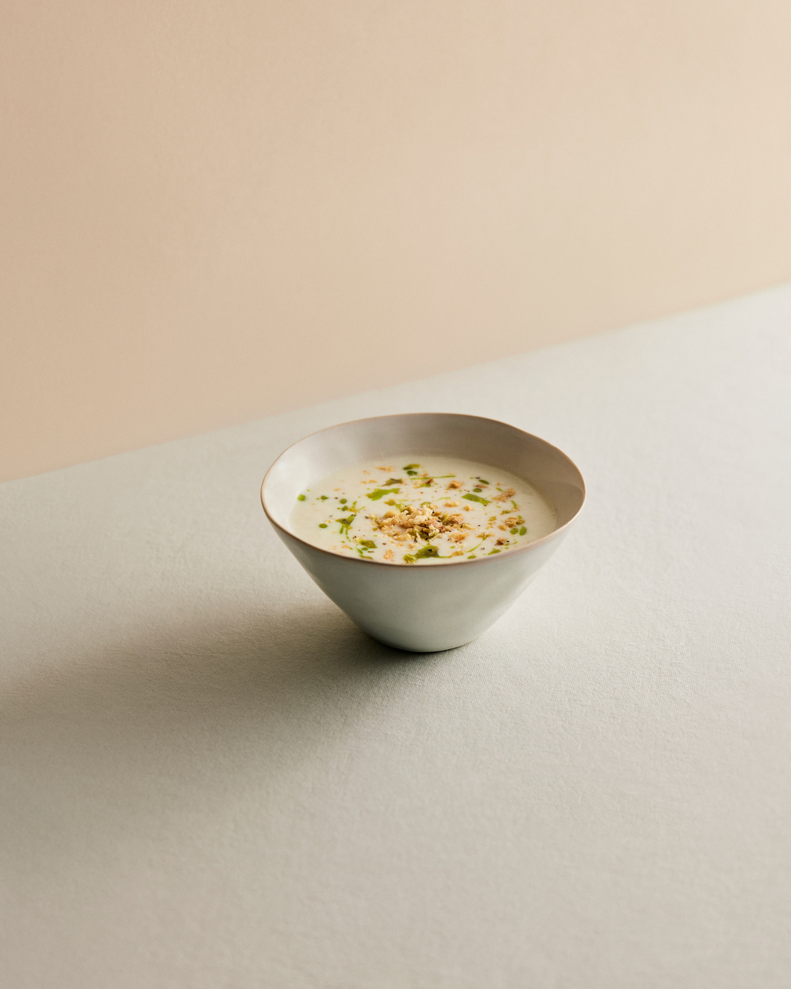 Bowl of creamy soup, decorated with herbs and nuts, on a light background.