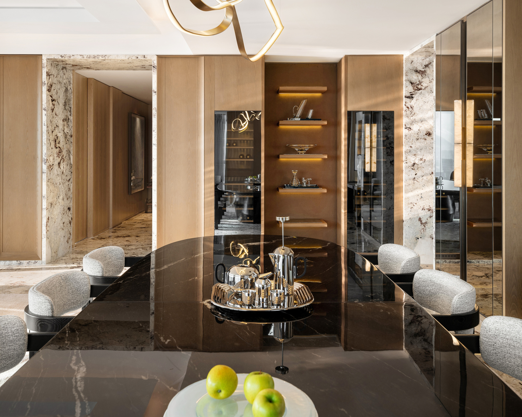 Cucina moderna con tavolo in marmo nero, illuminazione dorata e dettagli decorativi come mele verdi e una teiera lucida.