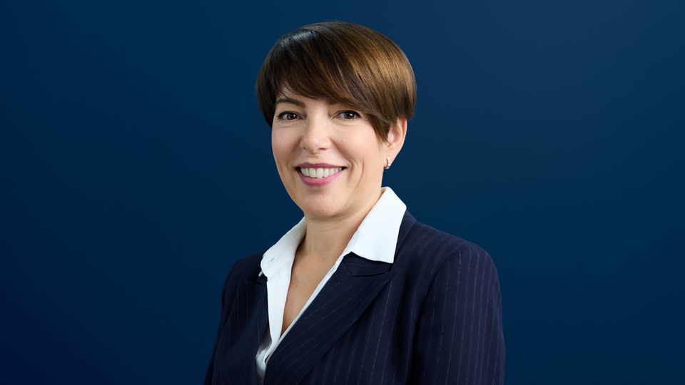 Portrait of a woman in a business outfit against a dark blue background.