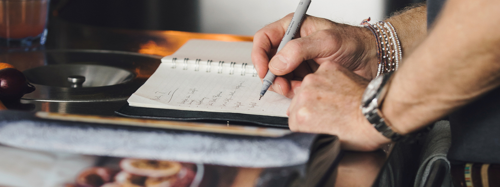Person writing recipe notes in a kitchen with fire in the background.