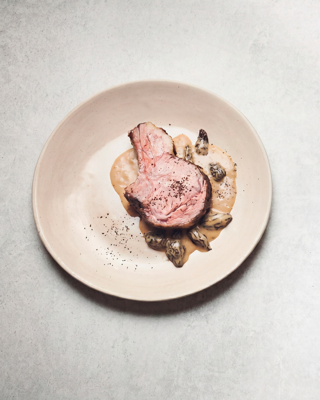 Ein Tellergericht mit zartem Fleisch, cremiger Sauce und Morcheln, minimalistisch angerichtet.